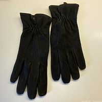 Pair of black suede gloves laid flat, showing front side with gathered elastic detail at wrist and smooth fingers.