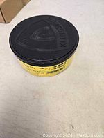 Round plastic container with black lid embossed 'Kronenflex' containing cutting wheels.