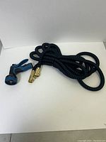Full view of extendable garden hose coiled with spray nozzle attached showing braided black and blue design with brass fittings.