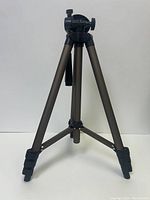Front view of the tripod fully extended showing three brown telescoping legs with black foot grips and a black center support.