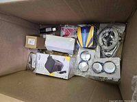 Top view of box showing vacuum cleaner, adhesive tape, mirror covers, metal hardware, red and white reflectors, and black cylinder item.