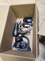 Open cardboard box with black hair dryer, black headphones with red accents, and power adapters inside