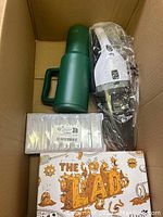 Top view of box showing green thermos jug, black hairdryer in plastic, plastic container of craft supplies, and a box labeled The Lab