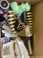 View showing black and gold Egyptian-style costume mask with striped headdress, white sports gloves, and craft paint jars inside the box