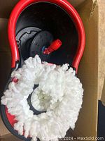 Red and black bucket or container with coiled white foam or packing inside, placed in cardboard box.