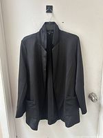 Front view of medium black blazer hanging on a hanger, showing design and pockets.
