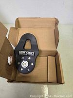 Photo of the Ranger pulley inside an open cardboard box showing the product with logo and metal axle detail.
