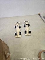 Two white Velocity model racing cars next to each other on a light grey floor.