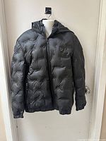 Front view of black Vogtide puffer coat with visible zippered pockets and logo on chest.