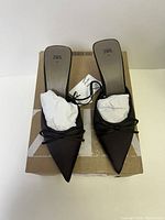 Top-down image of the black Zara pointed toe mules on a cardboard box, showing the left and right shoe with white tissue paper stuffed inside and Zara branding on the insole.