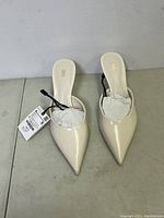 Front view of the Zara pointed-toe heels, showing creamy off-white color and pointed toe shape, with original tags attached to one shoe.