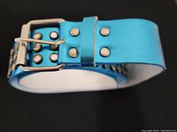 Close-up of turquoise blue belt showing metallic sheen, silver-tone studs in three rows, and silver-tone buckle with prong.