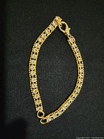 Full view of 5-inch gold-tone bracelet with clear jewels on black background.
