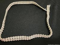 Full view of the necklace shows silver-tone setting and clear round crystal stones laid out on a black fabric background.