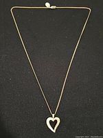 Full view of gold-finish necklace with heart pendant on black background