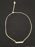 Full view of the delicate gold finish necklace showing the chain and the bar pendant with adjustable chain and charm.