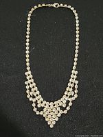 Full view of the faux diamond necklace laid out on a black background, showing the overall shape and design of linked stones forming a bib-style pattern.