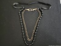 Full view of black beaded and chain necklace laid flat on black background.