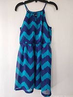 Full front view of blue and navy chevron patterned dress hanging on black hanger against white background.