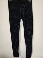 Full front view of black women's pants with a subtle abstract pattern hung on a hanger against a white background.