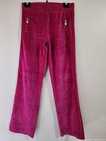 Full length front view of pink velour pajama pants hanging on a black hanger against a white wall.