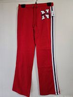 Full front view of red sports pants hanging with visible drawstring and large 'N' with 'New York' logo on upper thigh