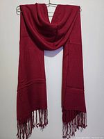 Front view of the red pashmina scarf hanging on a wall, showing its rectangular shape and fringed ends.