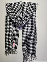 Full view of the large black and white houndstooth scarf hanging on a wall showing the full shape and fringed ends.