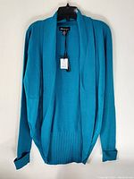 Front view of turquoise sweater jacket hanging on black hanger showing ribbed shawl collar, long sleeves with cuffs rolled up, and sewn-in brand tag with price attached.