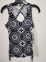 Front view of women's sleeveless top with black and white geometric pattern hung on black plastic hanger.