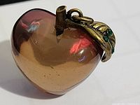 Clear view of smoky glass heart-shaped pendant with gold-tone leaf charm and green rhinestones.