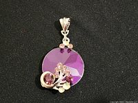 Front view of a silver-tone pendant with a large faceted circular purple gem and a swirl of purple and pink rhinestones at the bottom.