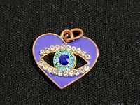 Close-up of heart-shaped pendant with purple enamel and rhinestone evil eye design on front.