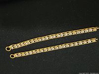 Two gold-tone pendants set with clear square rhinestones placed side by side on black fabric background.