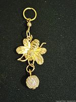 Full view of the gold tone bee pendant with hanging jewel against black background.