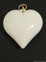 Front view of white glossy heart-shaped pendant with gold-tone loop on black background