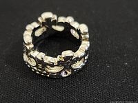 Close-up photo of small silver ring showing detailed raised floral and geometric pattern around the band, on black background.