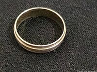 Close-up photo of the gold finished ring showing the flat top view with detailed strips and shiny metal finish.