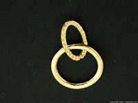 Close-up photos of a gold fin ring featuring two interlocked oval bands with hammered texture, displayed on a black fabric background.