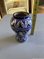 Blue and white glazed ceramic vase with decorative pattern, about 6 inches tall, shown with measuring tape for scale.