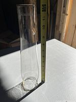 Side view of the clear glass chimney standing upright on a white surface with measuring tape showing height around 12 inches. The 'Alladin' brand etching near the top is visible.