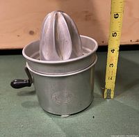 Full assembled mechanical juicer showing aluminum container, juicing cone, and attached handle with measurement tape showing height.