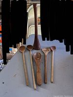 Photo showing five wooden spoons of different shapes and one tall wooden pestle, all appearing antique and well-used.