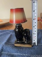 Side view showing two black glass cats and the red gradient lampshade with measuring tape showing around 4 inches height.