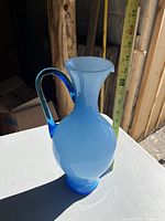 Blue glass water pitcher approximately 14 inches tall, two-toned blue with a curved handle and spout, placed on a white surface with a measuring tape showing height.