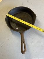 Cast iron frying pan with measuring tape showing approximately 9 inches diameter across the top.