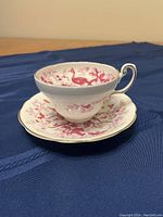 Teacup resting on matching saucer, showing the pink patterned design and gold trim on both items.