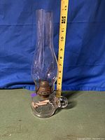 Oil lamp with tall glass chimney, photographed against a blue backdrop with a measuring tape showing approximately 13 inches tall.