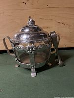 Side view of vintage glass ice bucket with ornate hand forged aluminum frame and lid with floral design