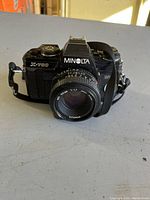 Front angle view of Minolta X-700 with 50mm lens and strap on table under natural light showing camera body and lens details.